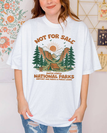 Woman wearing a white 'Not For Sale - United States National Parks' shirt with a retro graphic of national park woods and a tent.