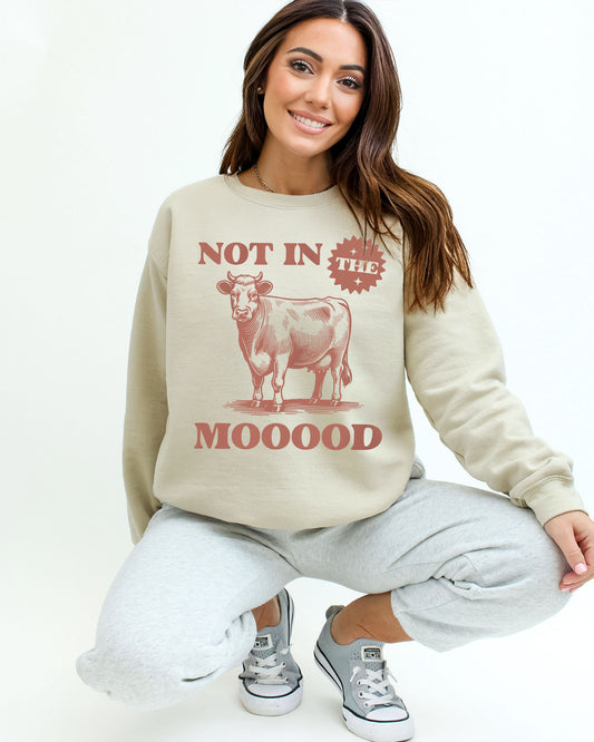 Woman wearing a sand beige sweatshirt featuring a retro cow grahic and the quote 'Not In The Mooood'.