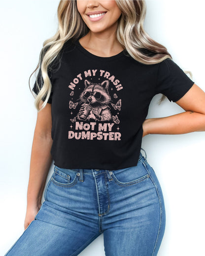 Woman wearing a black 'Not My Trash Not My Dumpster' crop top with a funny retro raccoon drinking coffee graphic.