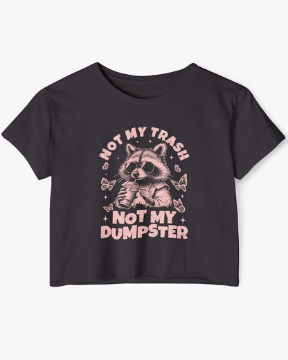Flat lay of a black 'Not My Trash Not My Dumpster' crop top featuring a funny retro raccoon drinking coffee graphic.