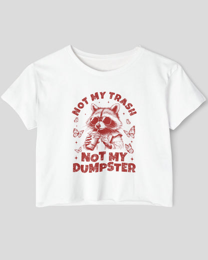 Flat lay of a white 'Not My Trash Not My Dumpster' crop top featuring a funny retro raccoon drinking coffee graphic.