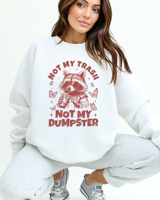 Woman wearing a white 'Not My Trash Not My Dumpster' sweatshirt with a funny retro raccoon drinking coffee graphic.