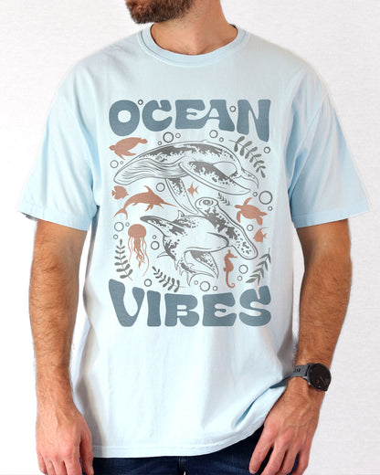 Man wearing a chambray-colored 'Ocean Vibes' t-shirt with a retro sea life collage graphic.