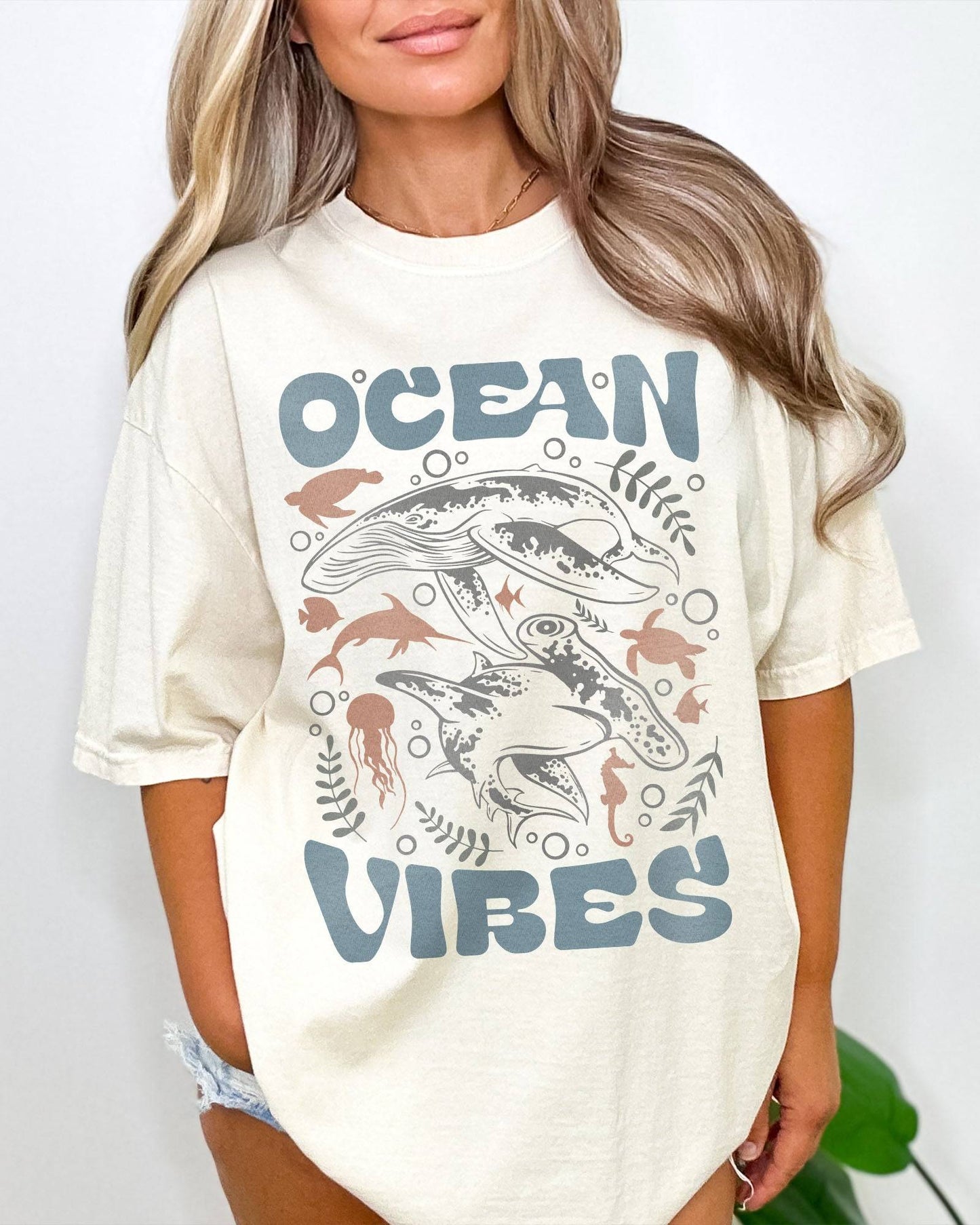 Woman wearing an ivory-colored 'Ocean Vibes' t-shirt with a retro sea life collage graphic.