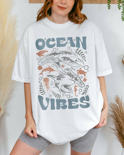 Woman wearing a white 'Ocean Vibes' t-shirt with a retro sea life collage graphic.