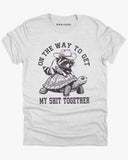 Flat lay ash gray 'On The Way to Get My Shit Together' t-shirt featuring a funny retro raccoon riding a slow-moving turtle graphic.