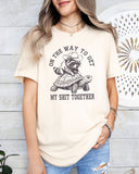 Woman wearing a natural 'On The Way to Get My Shit Together' tee featuring a funny retro raccoon riding a slow-moving turtle graphic.