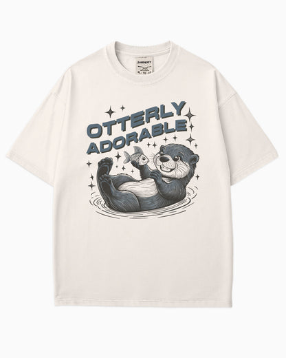 Flat lay ivory 'Otterly Adorable' shirt with a retro graphic of a happy otter holding a fish.