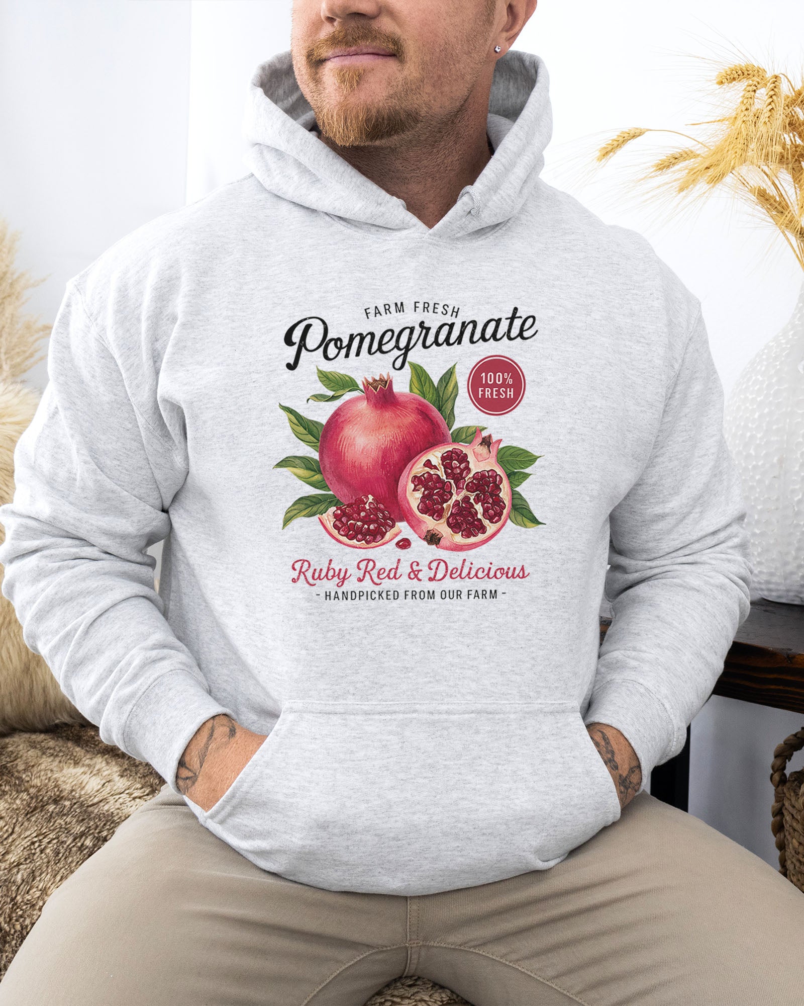 man wearing an ash hoodie featuring a vintage-style Pomegranate fruit label graphic with the text 'Pomegranate - Ruby Red & Delicious'.