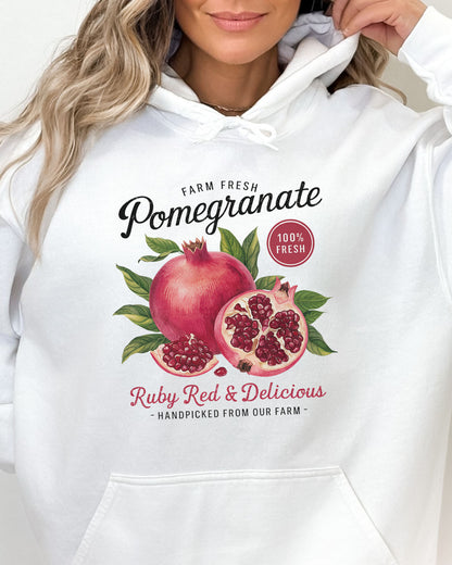 Close-up of a woman wearing a white hoodie with a vintage-style Pomegranate fruit label graphic and the text 'Pomegranate - Ruby Red & Delicious'.