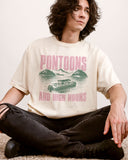 Man wearing "Pontoons And High Noons" shirt in ivory color with a retro graphic of a pontoon on a lake.