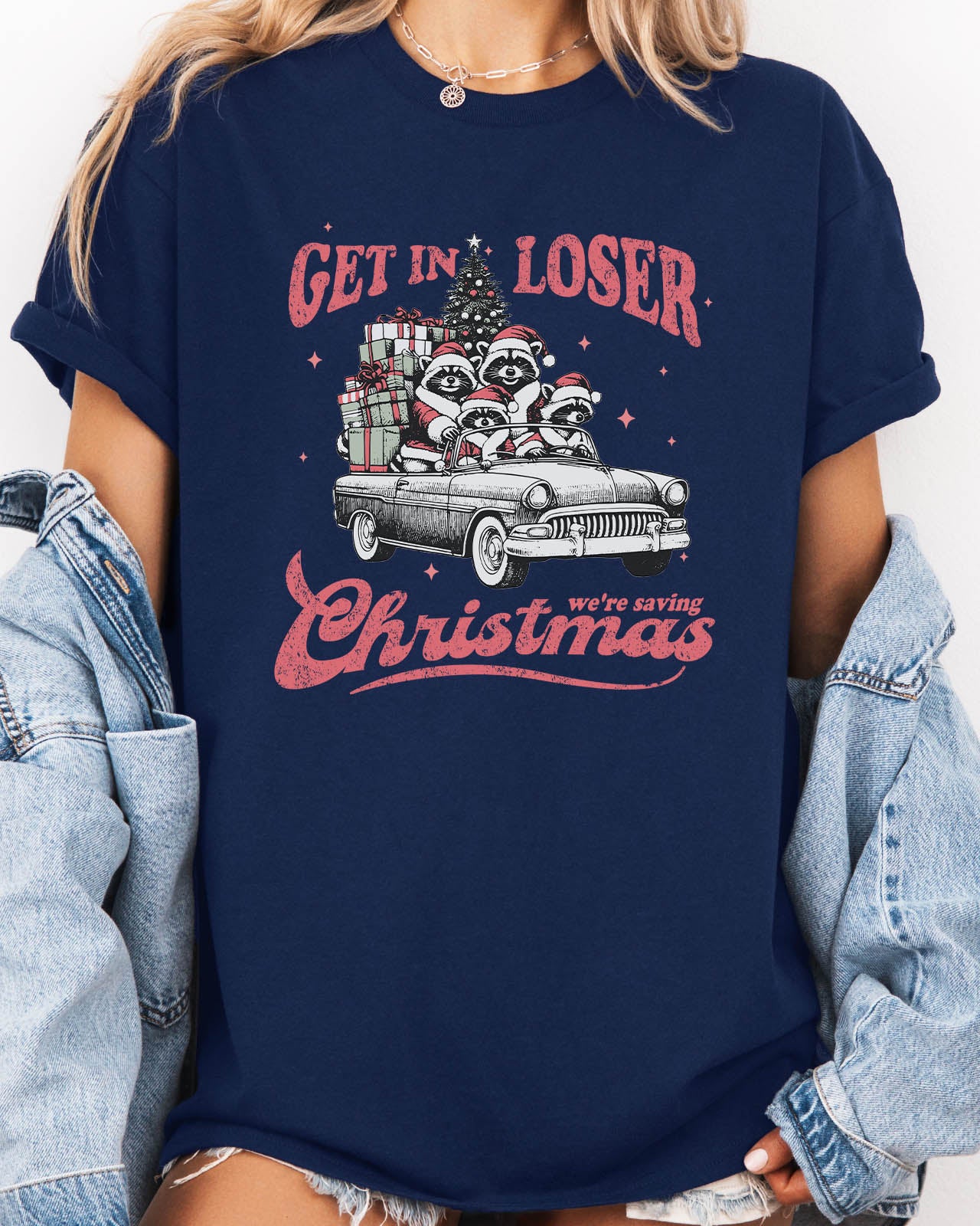 Woman wearing "Get In Loser We're Saving Christmas" shirt in navy blue color with a retro funny raccoon XMAS graphic