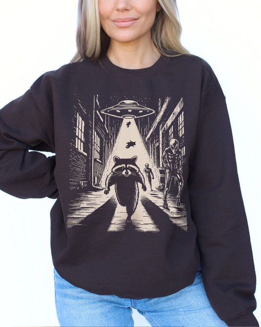 Woman wearing a dark chocolate sweatshirt with a retro graphic of a raccoon running from aliens.
