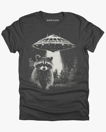 Flat lay dark heather 'Raccoon UFO' t-shirt featuring a funny graphic of a raccoon escaping a UFO abduction.
