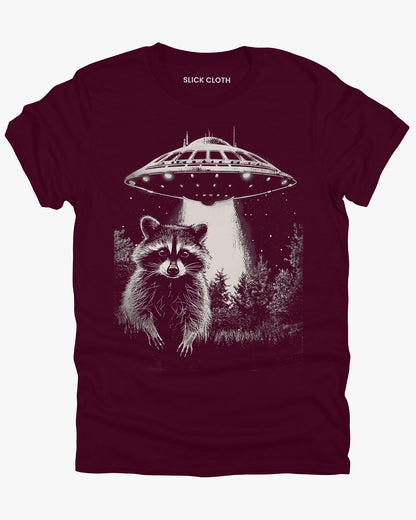 Flat lay maroon 'Raccoon UFO' t-shirt featuring a funny graphic of a raccoon escaping a UFO abduction.