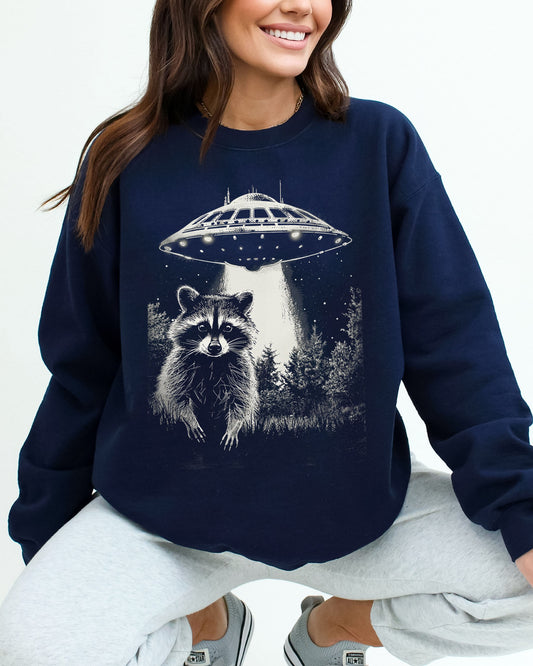 Model wearing navy color sweatshirt with 'Raccoon Escaping UFO Abduction' graphic design