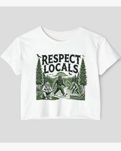Flat-lay white 'Respect Locals' crop top featuring a funny retro Bigfoot walking through the forest graphic.