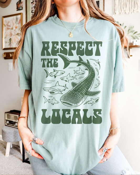 Woman wearing a bay-colored ‘Respect The Locals’ shirt with a retro graphic of whales, sharks, and fish.