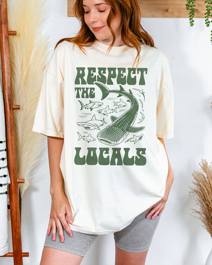 Woman wearing an ivory-colored ‘Respect The Locals’ shirt with a retro graphic of whales, sharks, and fish.