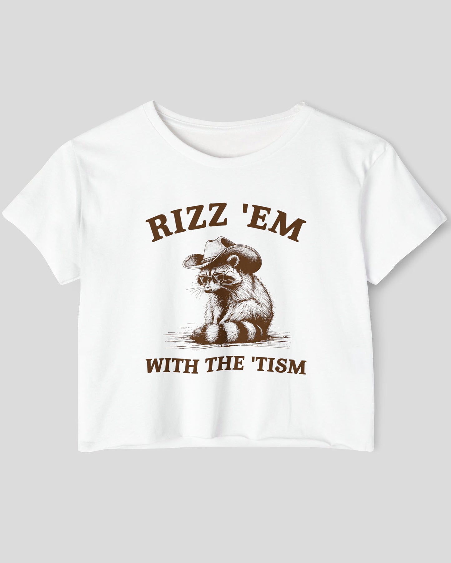 Flat-lay white 'Rizz Em With The Tism' crop top featuring a funny retro cowboy raccoon graphic.