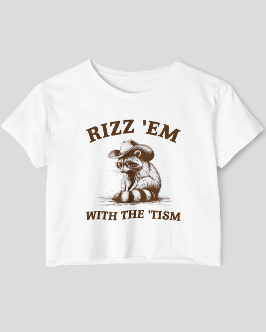 Flat-lay white 'Rizz Em With The Tism' crop top featuring a funny retro cowboy raccoon graphic.