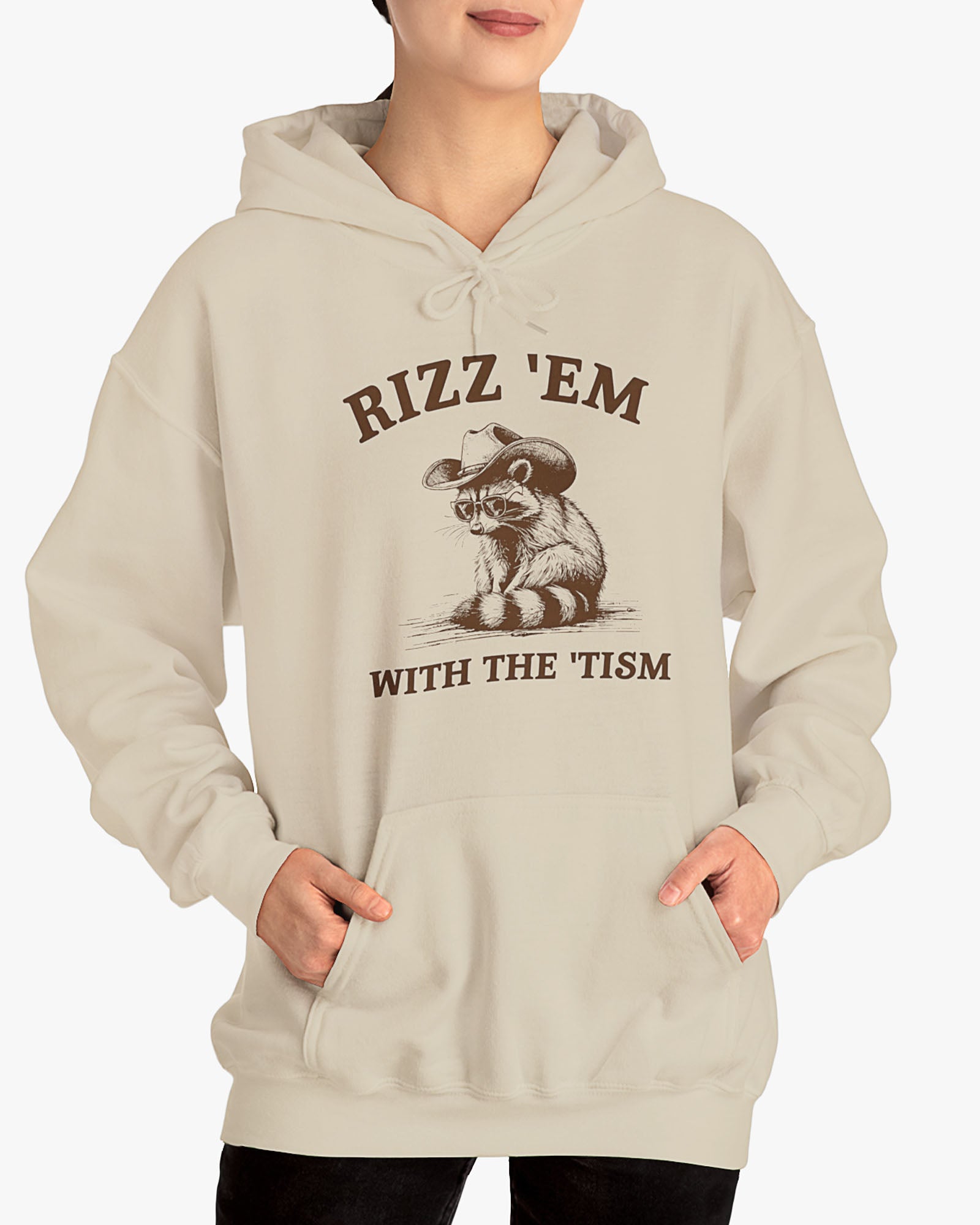 Woman wearing a sand beige Rizz ‘Em With The Tism Hoodie, featuring a retro cowboy raccoon graphic with a funny slogan.