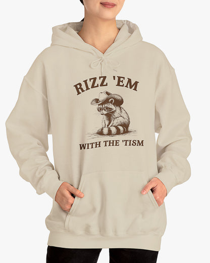Woman wearing a sand beige Rizz ‘Em With The Tism Hoodie, featuring a retro cowboy raccoon graphic with a funny slogan.