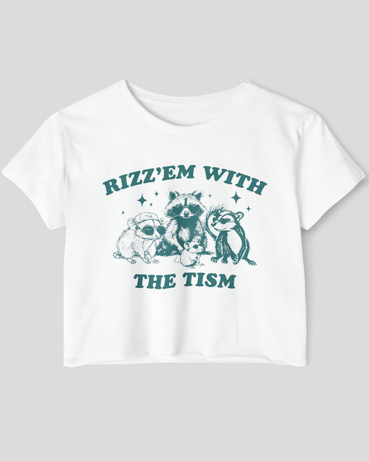 Flat lay white 'Rizz 'Em With The Tism' crop top featuring a funny retro raccoon gang graphic. Trendy women's graphic crop tee, retro aesthetic streetwear.