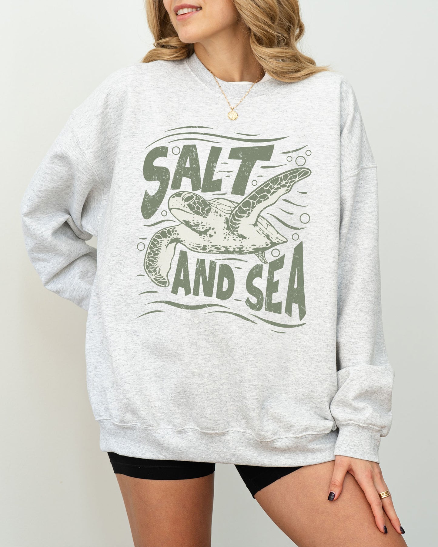 Model wearing ash color sweatshirt with 'Salt And Sea' graphic design