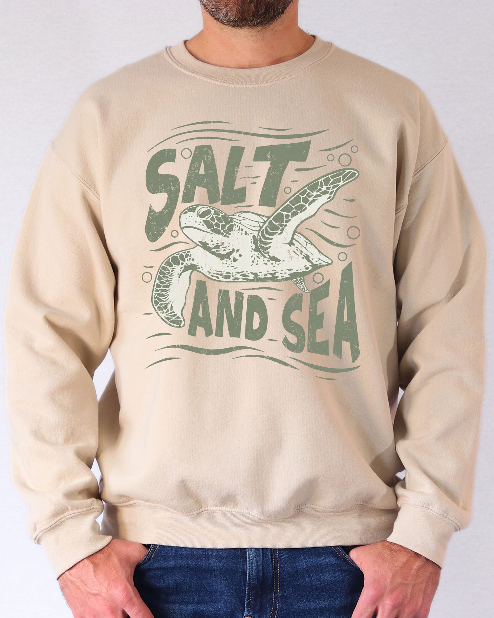 Model wearing sand color sweatshirt with 'Salt And Sea' graphic design