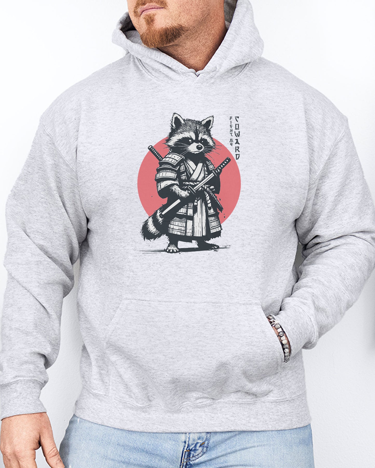 Man wearing an ash gray hoodie featuring a retro funny samurai raccoon graphic with the quote 'Fight Me Coward' in a Japanese-style font.