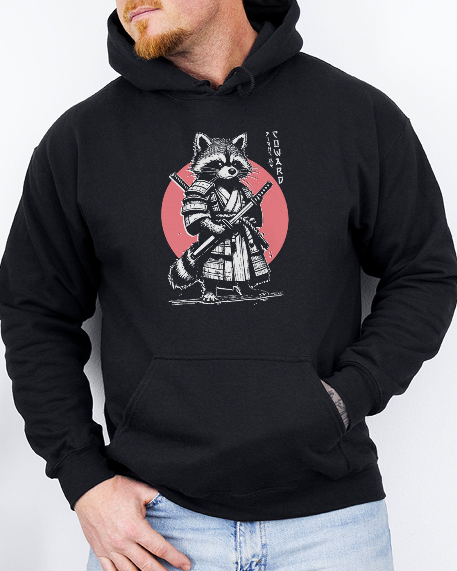 Man wearing a black hoodie featuring a retro funny samurai raccoon graphic with the quote 'Fight Me Coward' in a Japanese-style font.