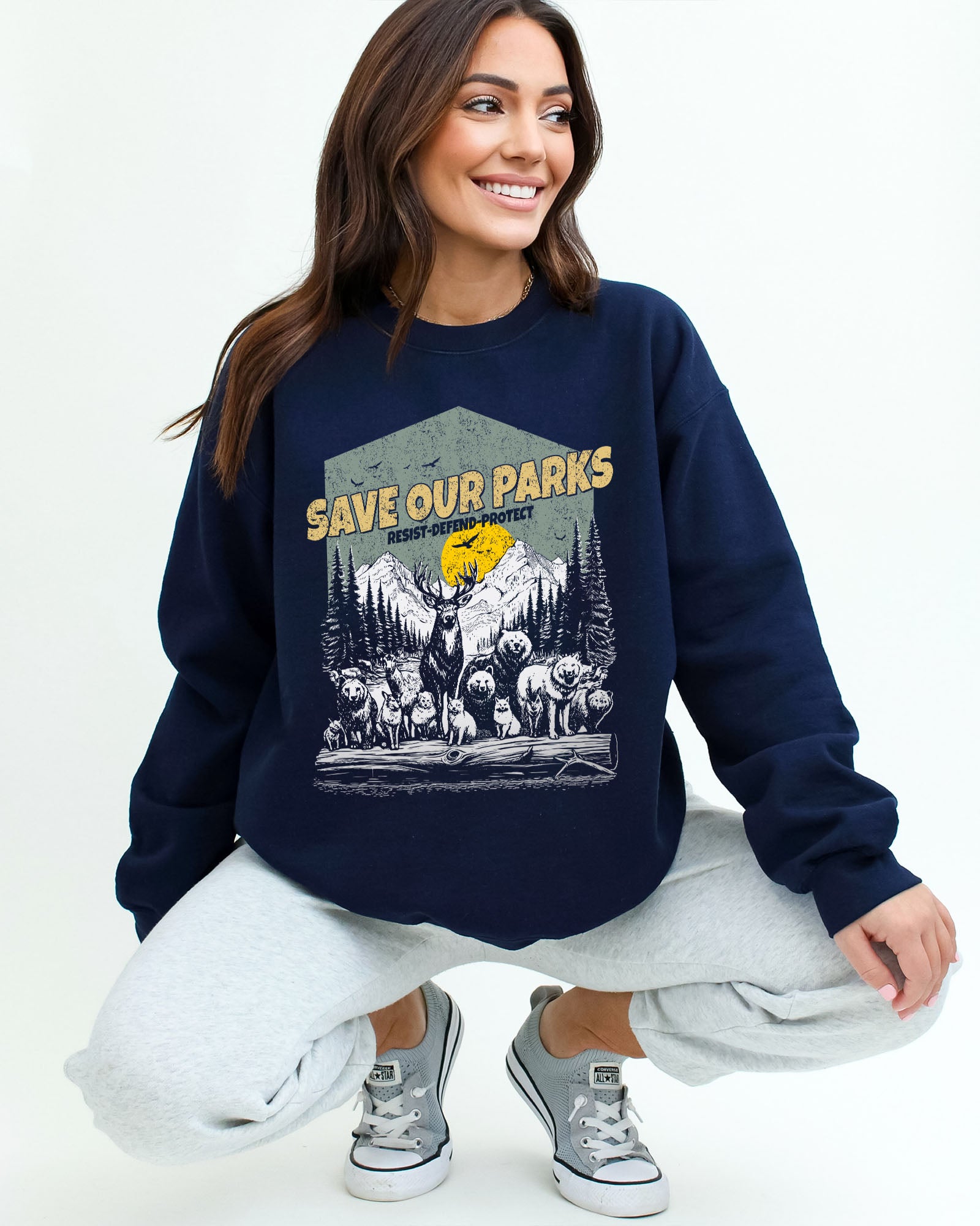 Woman wearing a navy blue sweatshirt with a retro wildlife design featuring animals lined up in a park and the quote 'Save Our Parks – Resist, Defend, Protect'.