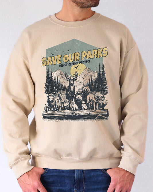 Man wearing a sand beige sweatshirt with a retro wildlife design featuring animals lined up in a park and the quote 'Save Our Parks – Resist, Defend, Protect'.
