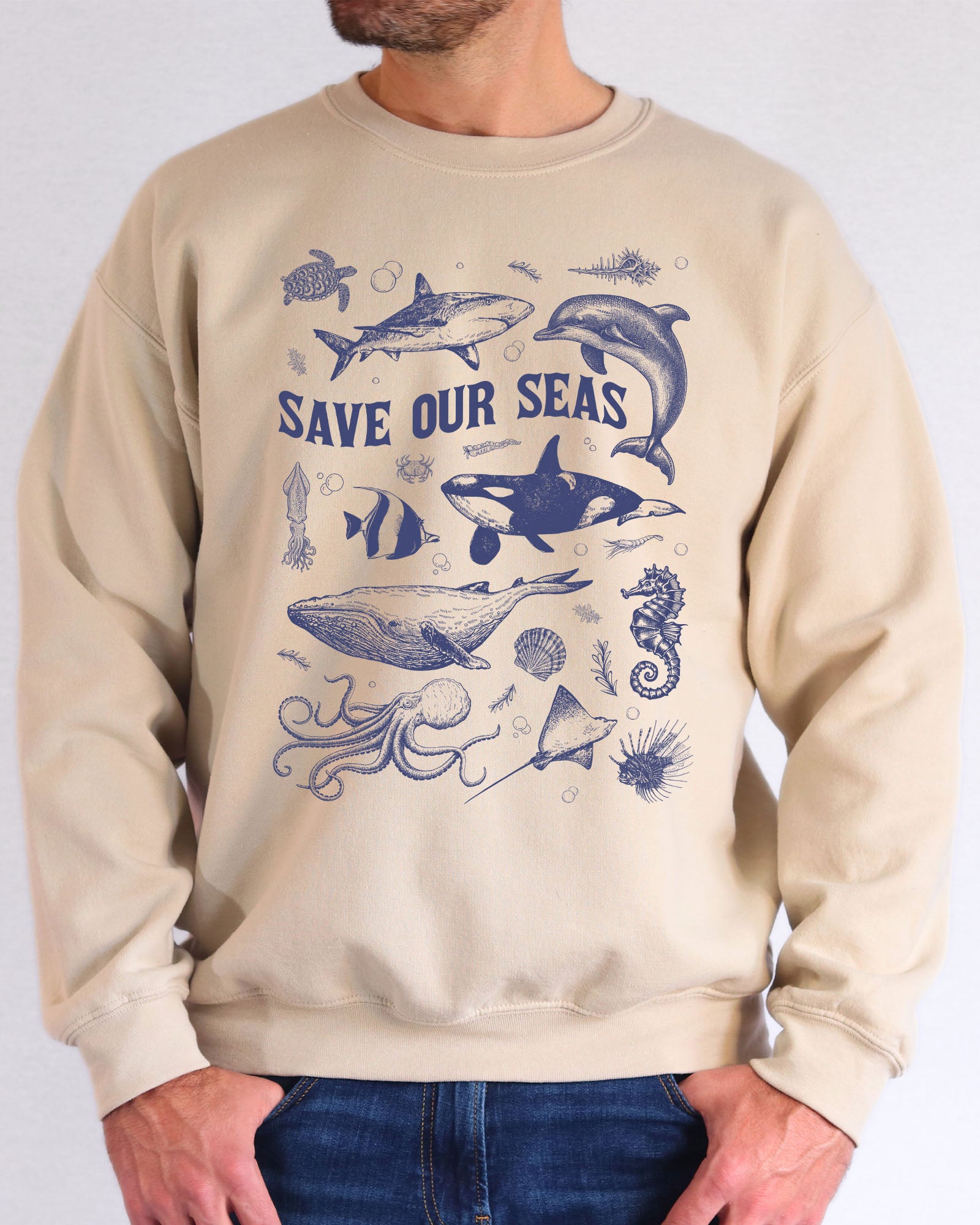 Model wearing sand color sweatshirt with 'Save Our Seas' graphic design