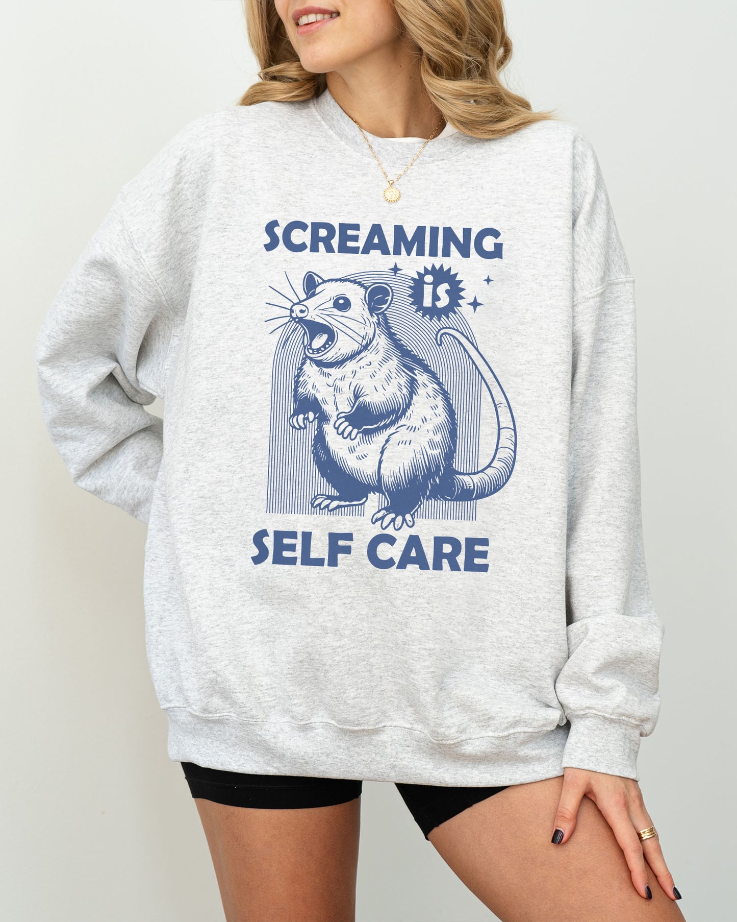Model wearing ash color sweatshirt with 'Screaming Is Self Care' graphic design