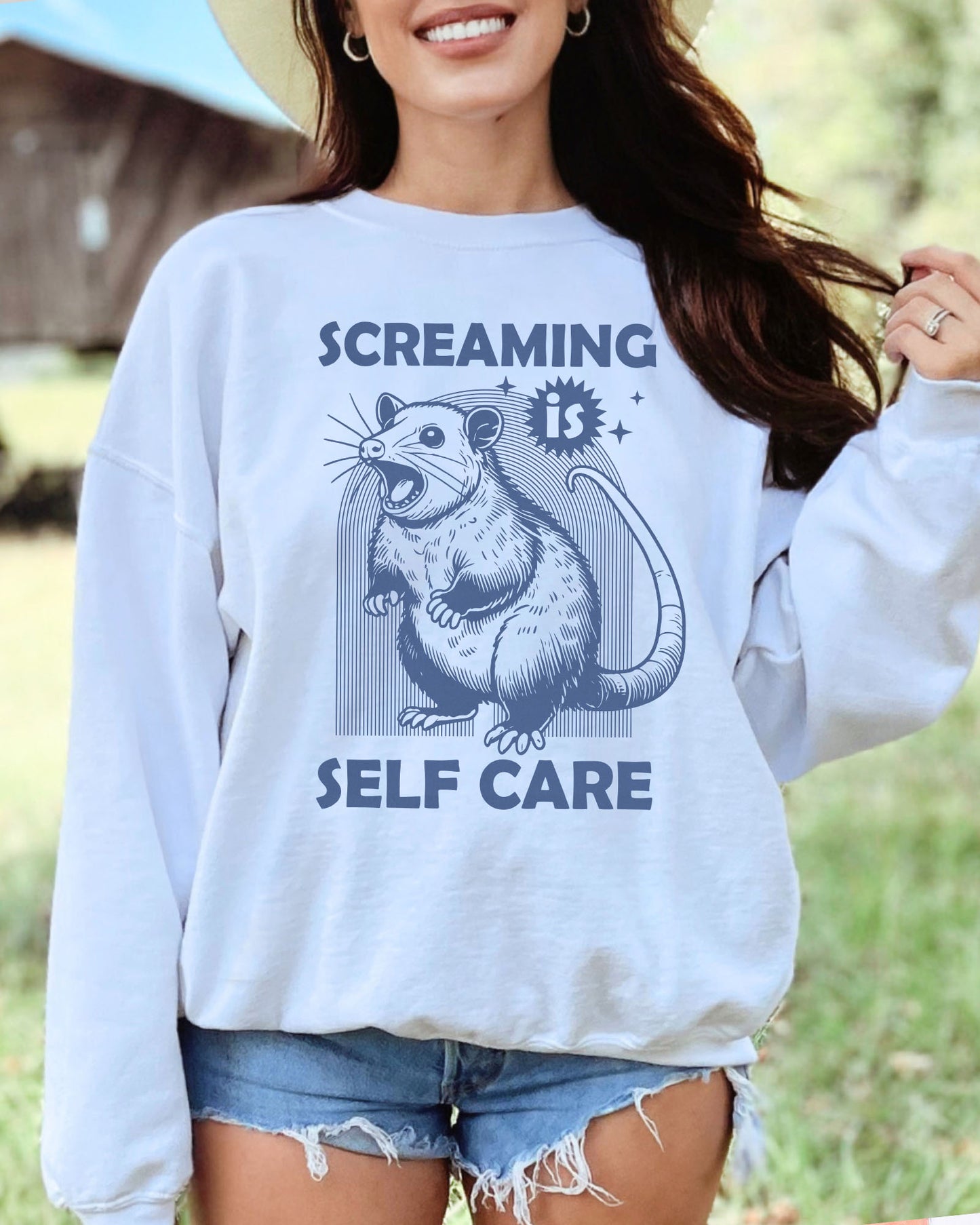 Model wearing white color sweatshirt with 'Screaming Is Self Care' graphic design