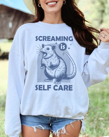 Model wearing white color sweatshirt with 'Screaming Is Self Care' graphic design