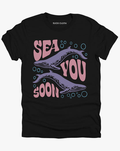 Flat lay of a black 'Sea You Soon' t-shirt featuring a retro whales and sea life graphic.