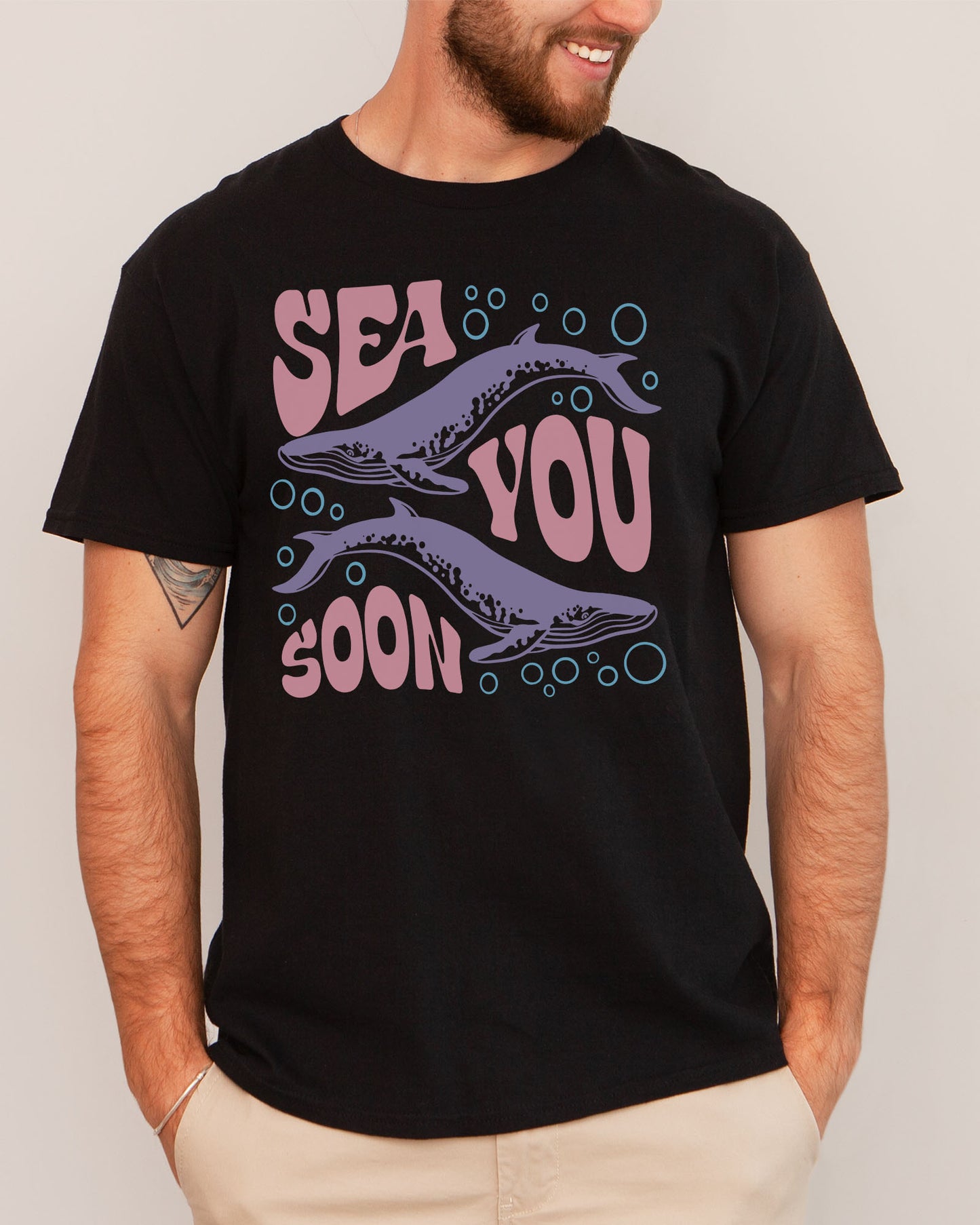 Man wearing a black-colored 'Sea You Soon' t-shirt with a retro whales and sea life graphic.
