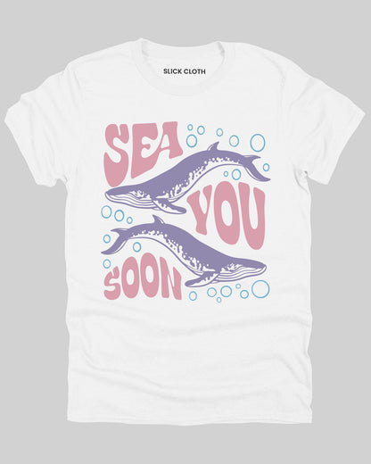 Flat lay of a white 'Sea You Soon' t-shirt featuring a retro whales and sea life graphic.