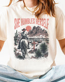 Close-up of woman wearing an ivory "She Humbles Herself" shirt with a retro graphic of a cowgirl riding a horse through the desert.