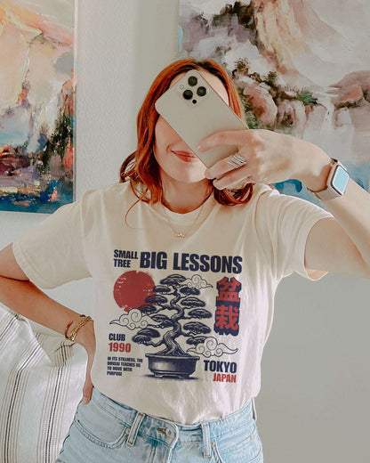 Woman taking a selfie of her in a white Small Tree Big Lessons Bonsai shirt with a retro Tokyo-inspired bonsai graphic.