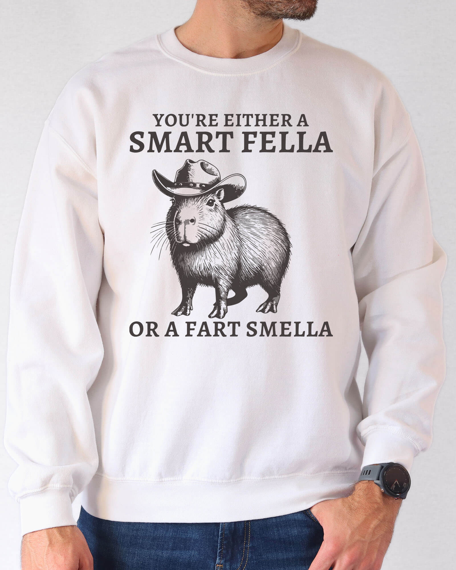 Man wearing a white sweatshirt featuring a funny retro cowboy capybara graphic and the quote 'You're Either A Smart Fella Or A Fart Smella'.