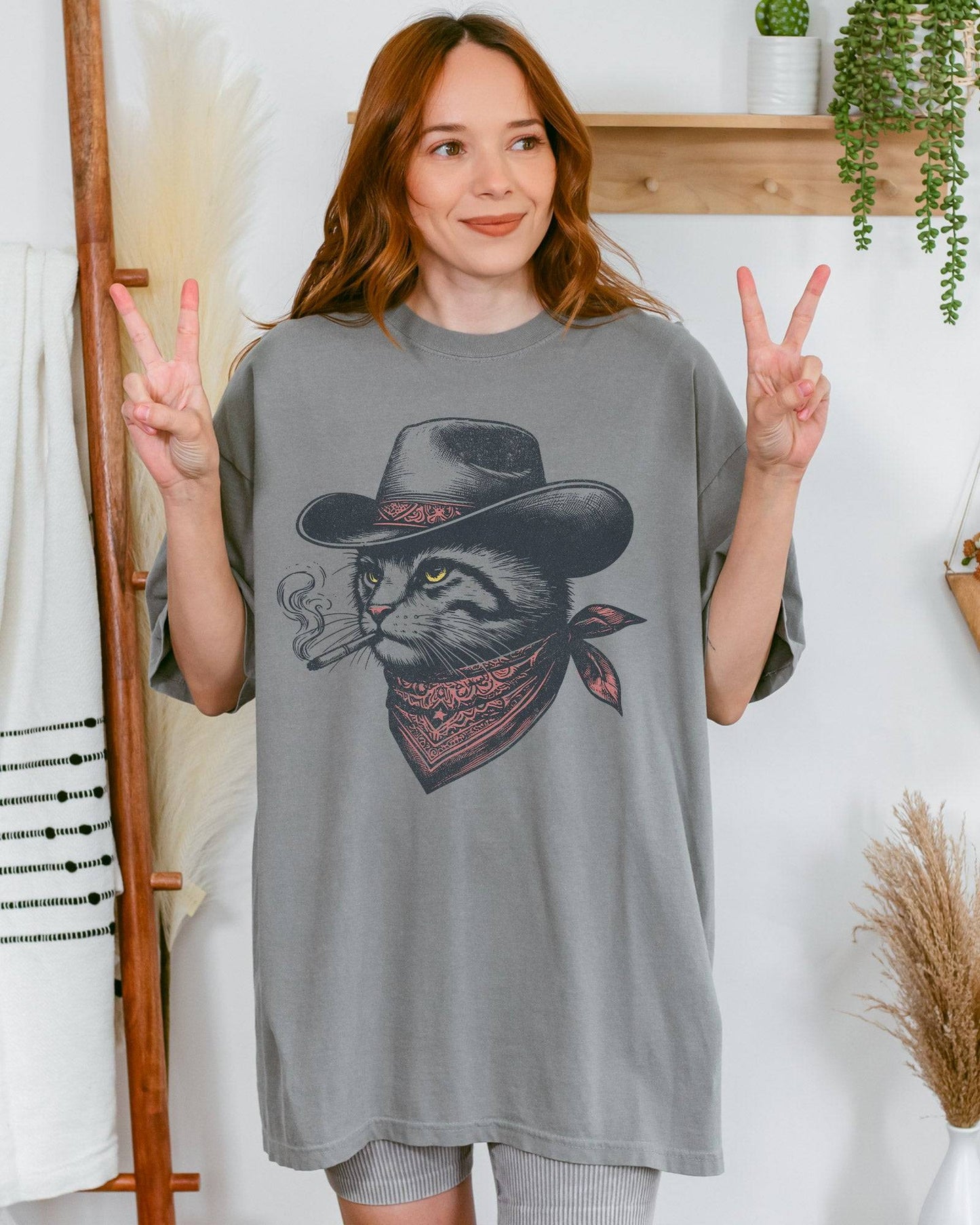 Woman wearing gray shirt with retro graphic of a smoking cowboy cat