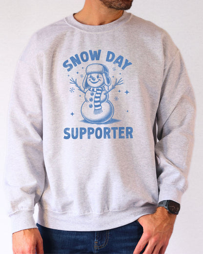 Model wearing ash color sweatshirt with 'Snow Day Supporter' graphic design