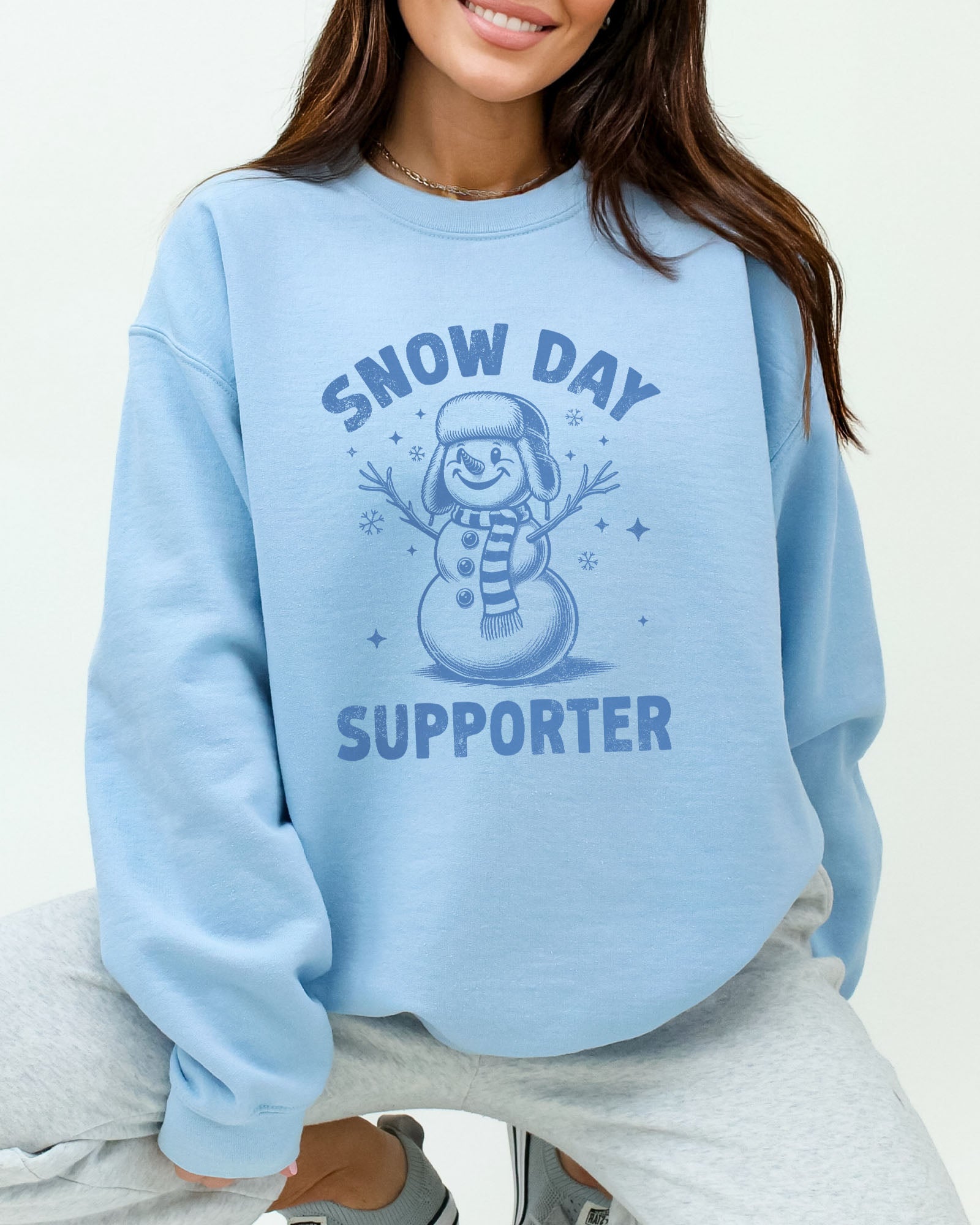 Model wearing light blue color sweatshirt with 'Snow Day Supporter' graphic design