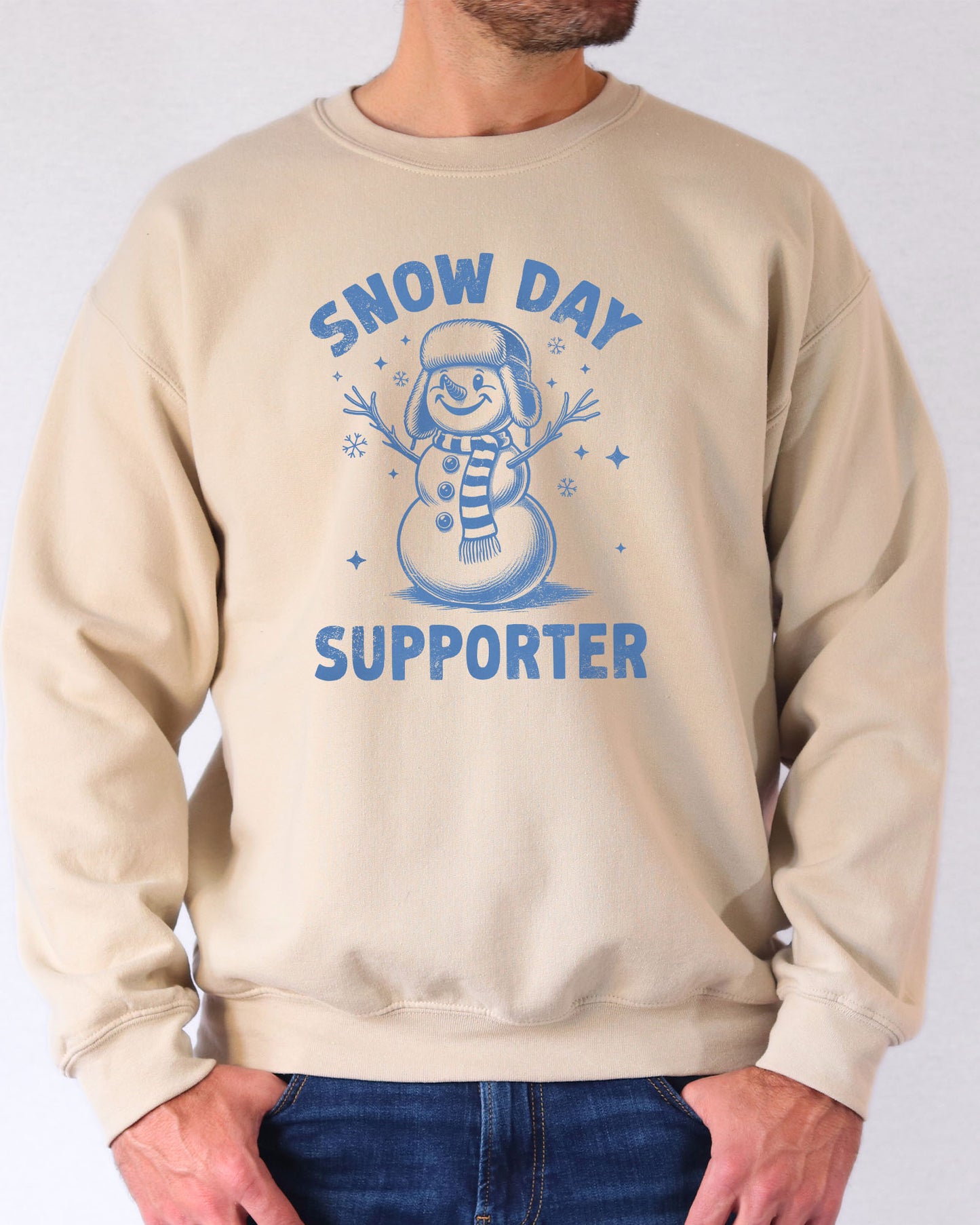 Model wearing sand color sweatshirt with 'Snow Day Supporter' graphic design