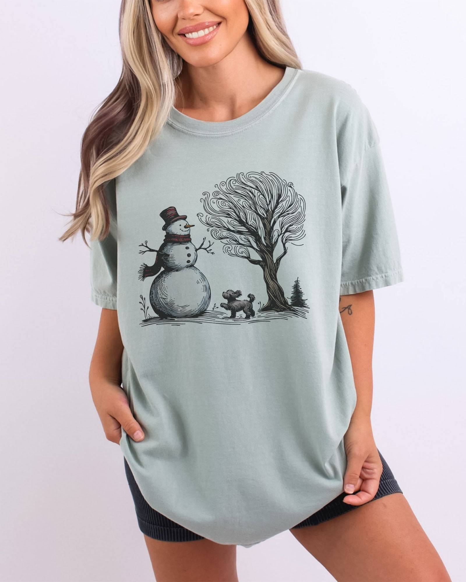 Model wearing bay color shirt with snowman and og winter landscape graphic design