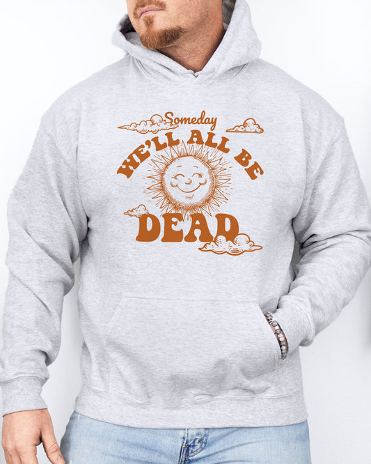 Man wearing an ash gray hoodie featuring a funny retro-style laughing sun graphic and the quote 'Someday We'll All Be Dead'.